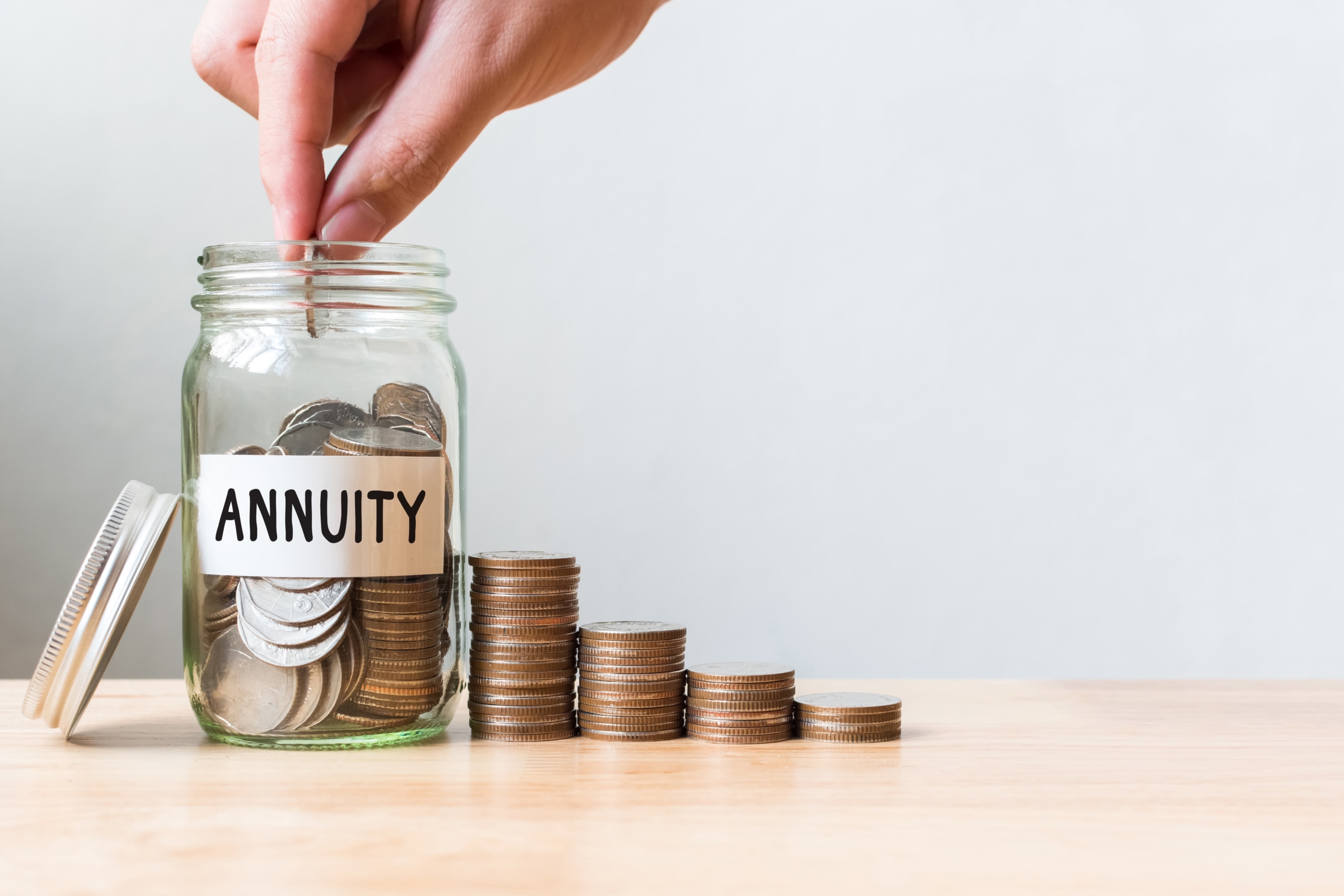 Hand putting coin in jar word annuity with coins stacked