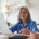 A woman in a blue shirt sits at a kitchen island with a calculator and forms.