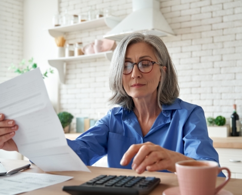 A woman in a blue shirt sits at a kitchen island with a calculator and forms.