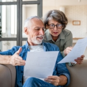 A senior couple compares papers on the couch.