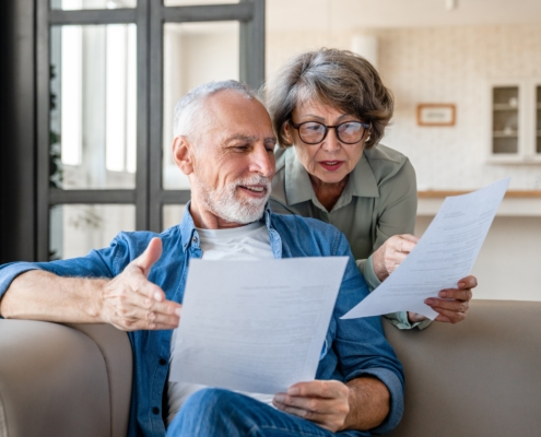 A senior couple compares papers on the couch.